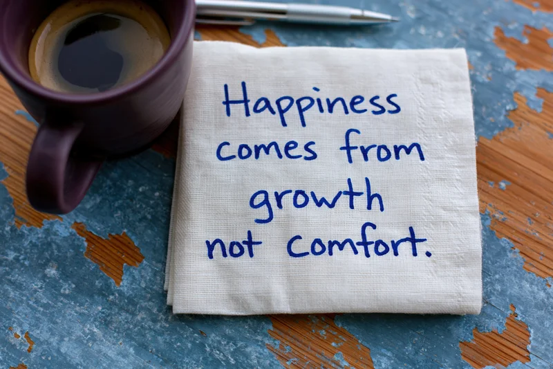 Handwritten motivational quote on a napkin beside a coffee mug on a rustic wooden table