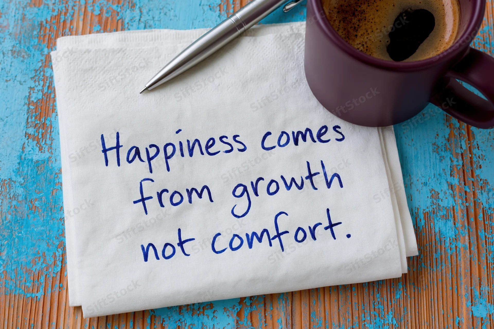 Handwritten motivational quote on a napkin with coffee mug and pen on a blue wooden table