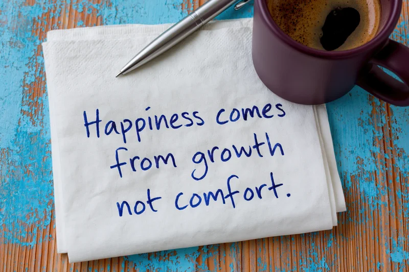 Handwritten motivational quote on a napkin with coffee mug and pen on a blue wooden table