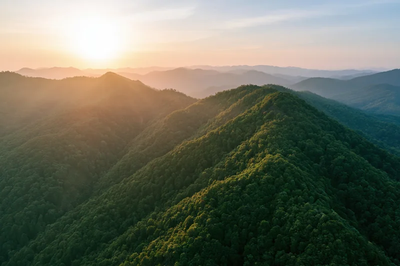 Aerial view of lush green mountain ridges layered into the distance at sunset