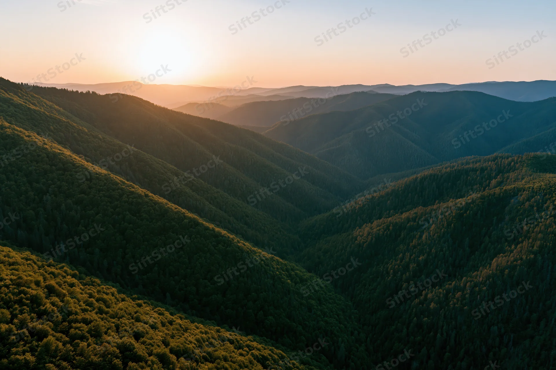 Aerial view of layered green mountain ridges at sunset