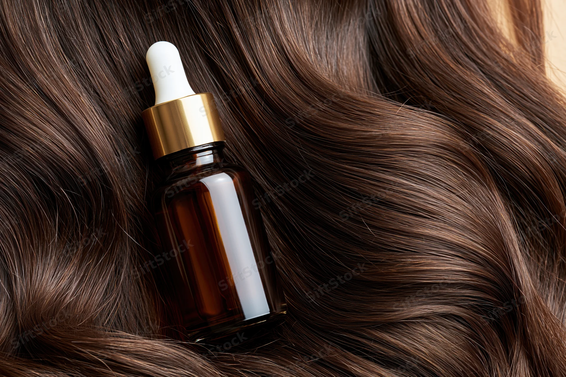 Amber glass dropper bottle resting on wavy brown hair