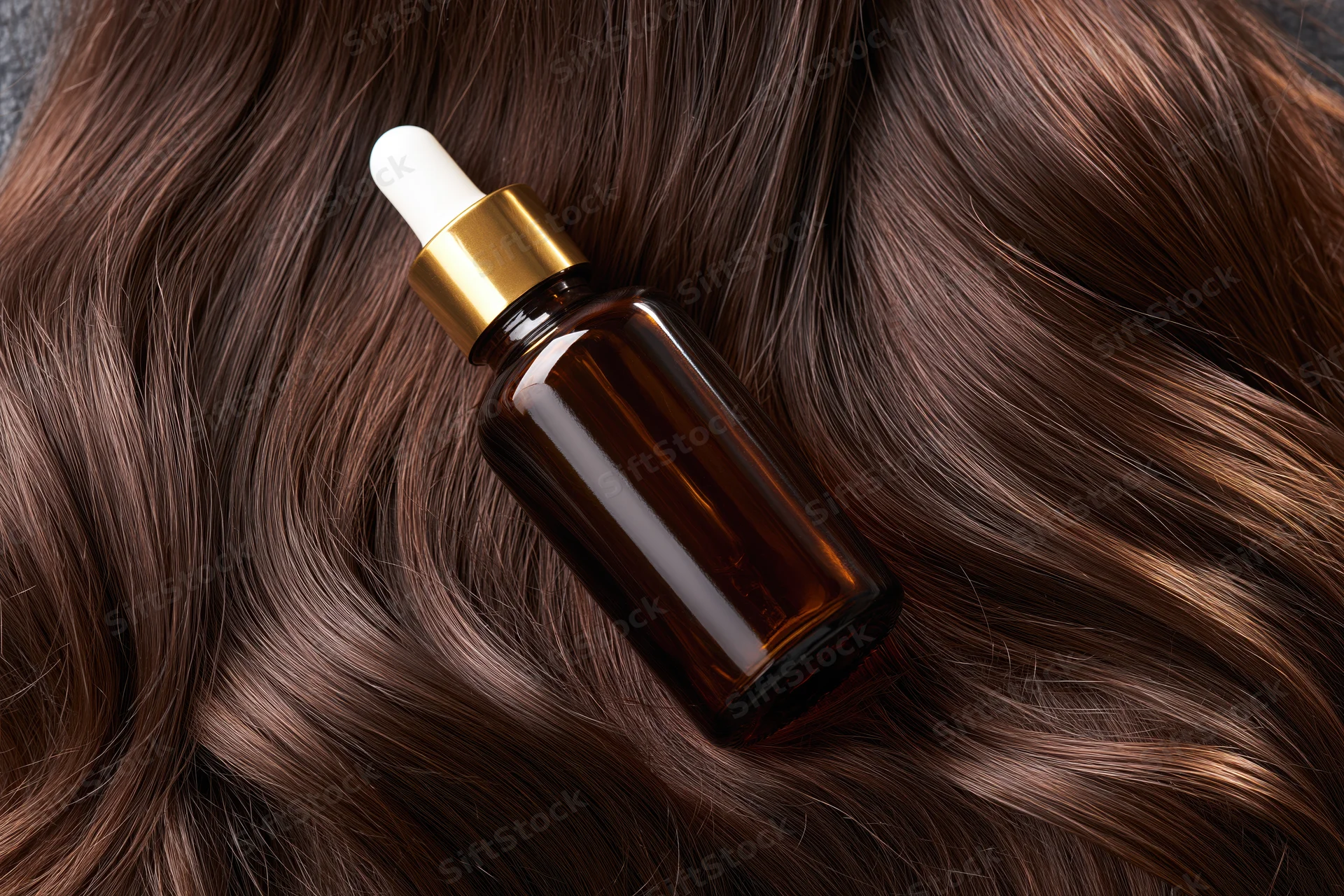 Amber glass dropper bottle resting on long wavy brown hair