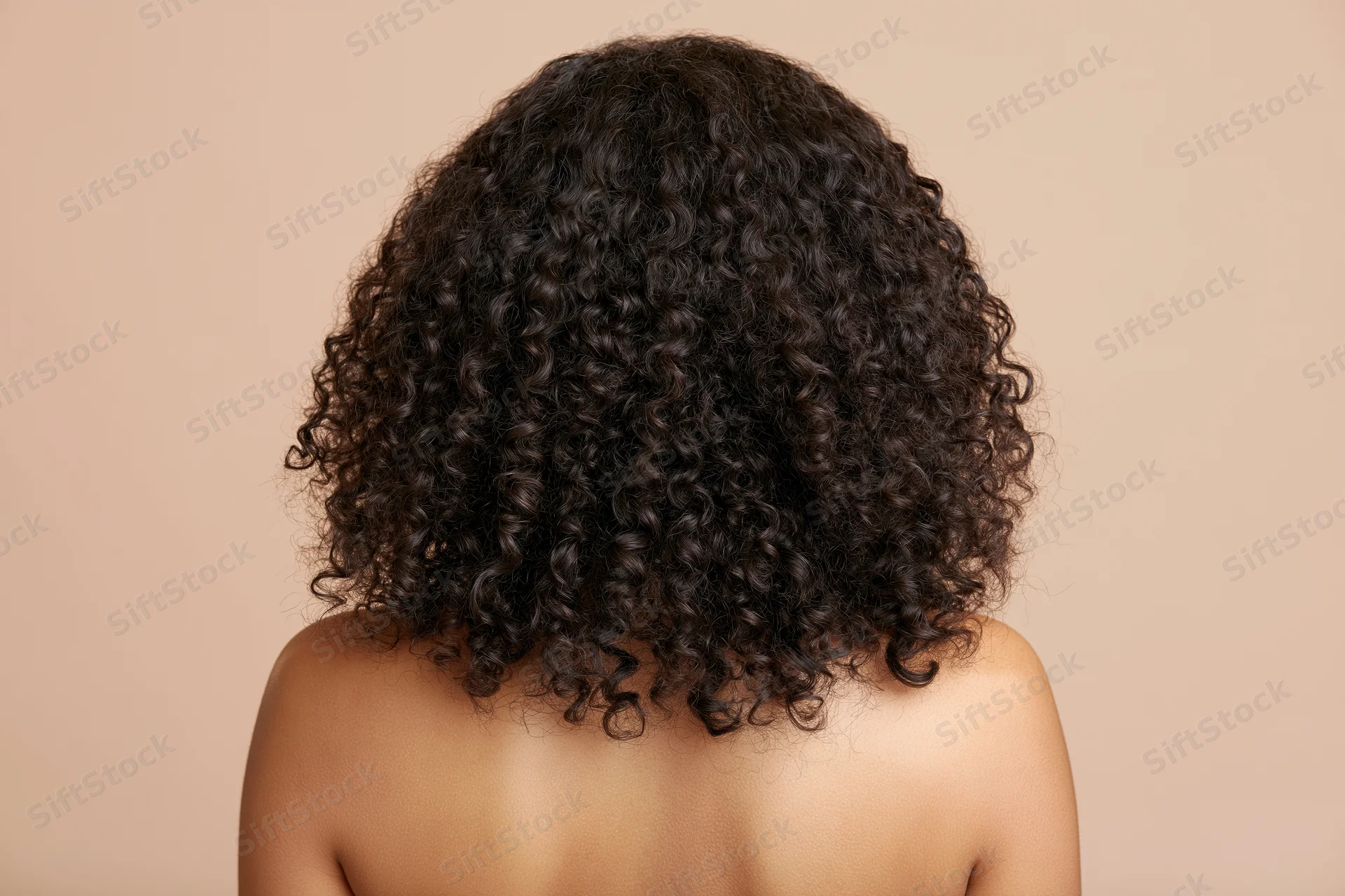 Back of a black woman with voluminous curly hair and bare shoulders against a neutral background
