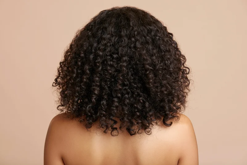 Back of a black woman with voluminous curly hair and bare shoulders against a neutral background