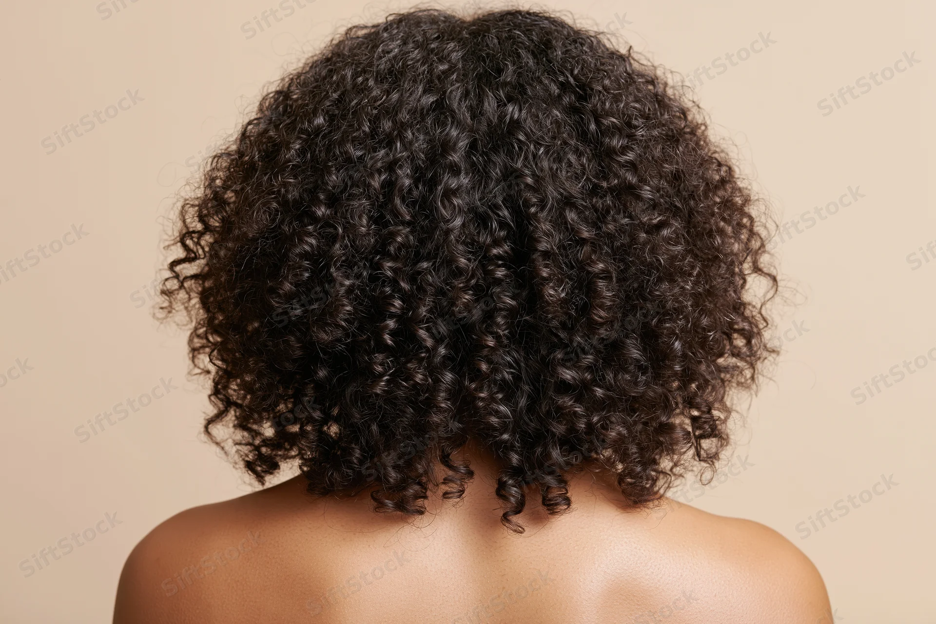 Back of a black woman with voluminous curly hair and bare shoulders against a neutral background