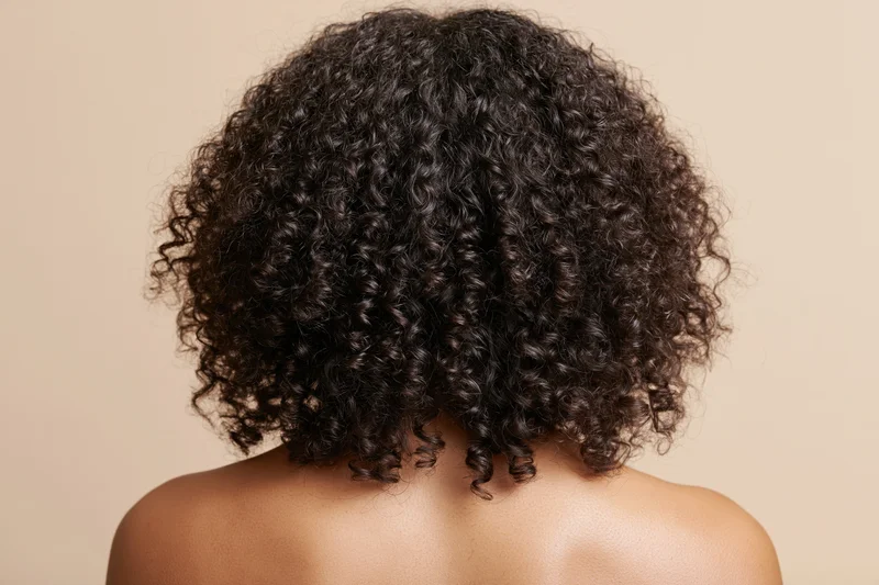 Back of a black woman with voluminous curly hair and bare shoulders against a neutral background