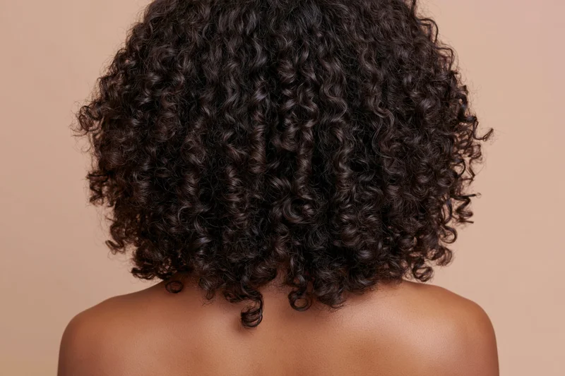 Back of a black woman with voluminous curly hair and bare shoulders in studio lighting