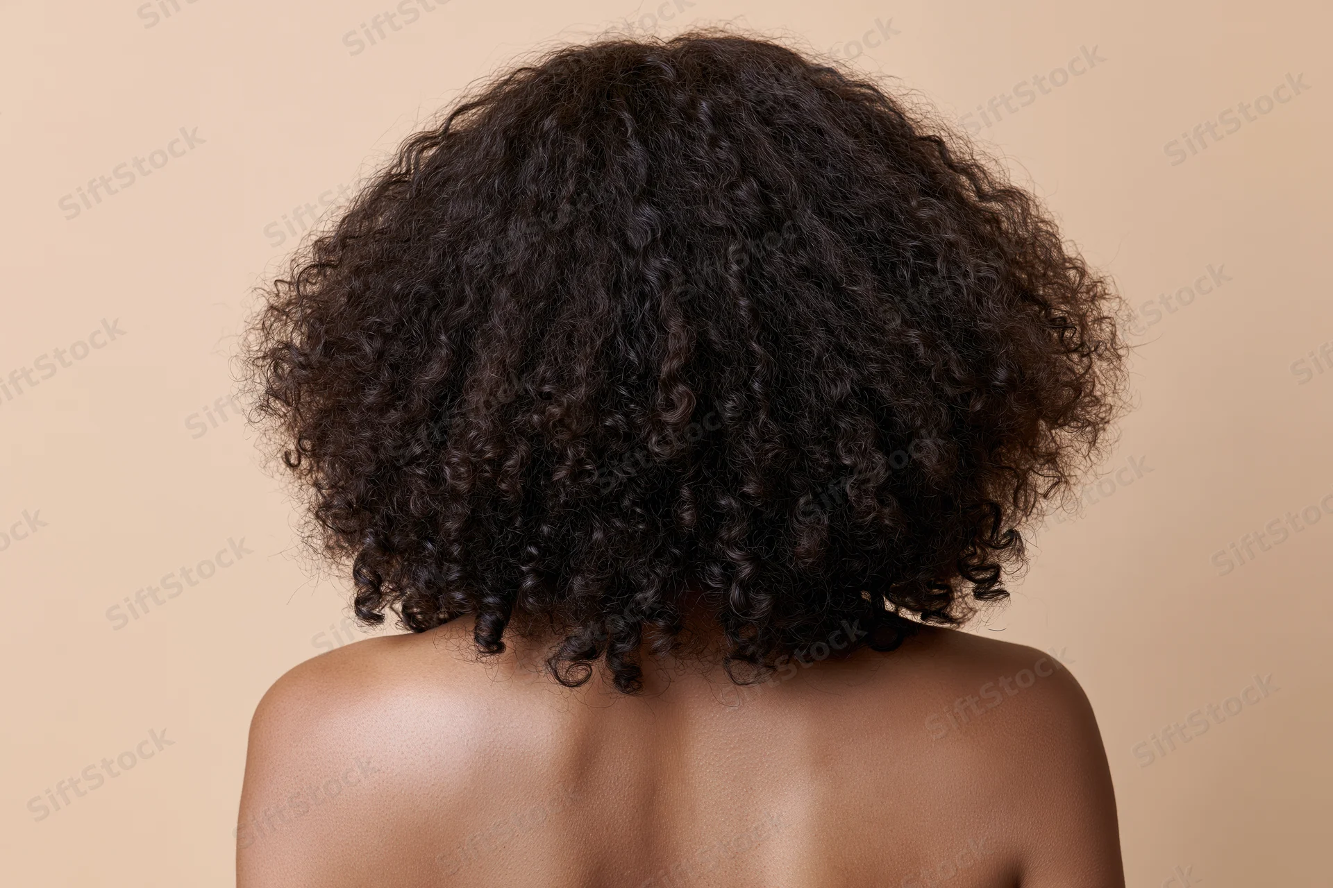 Back of a black woman with voluminous curly hair and bare shoulders against a neutral background