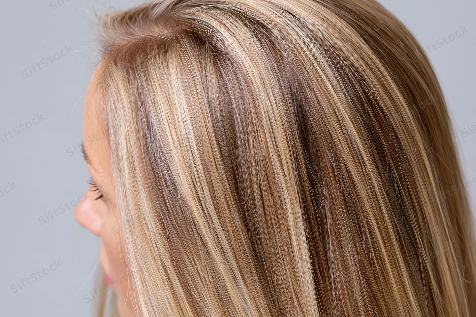 Side profile of a woman with long straight blonde hair showing highlights and smooth texture against a neutral background