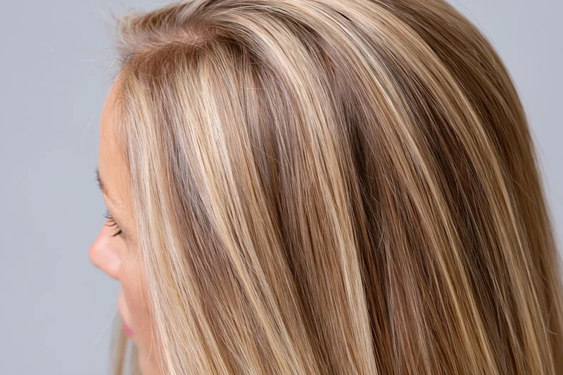 Side profile of a woman with long straight blonde hair showing highlights and smooth texture against a neutral background