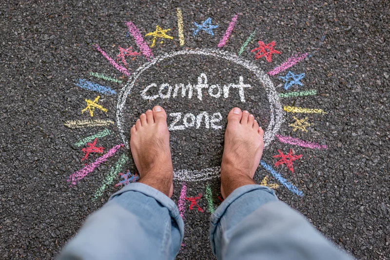 Bare feet standing inside a chalk-drawn circle labeled comfort zone on asphalt pavement