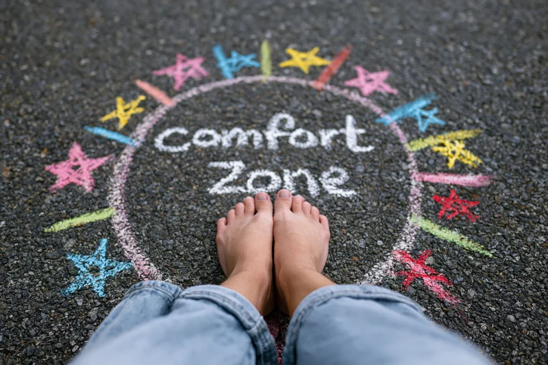 Bare feet standing inside a chalk-drawn circle labeled comfort zone on asphalt pavement