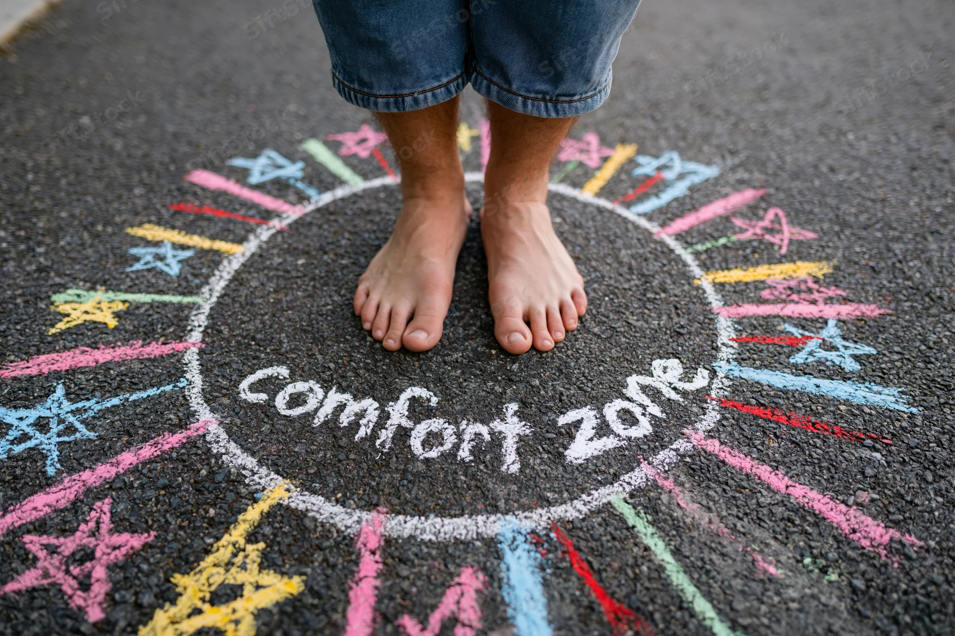 Bare feet standing inside a chalk-drawn circle labeled comfort zone on pavement with colorful stars radiating outward