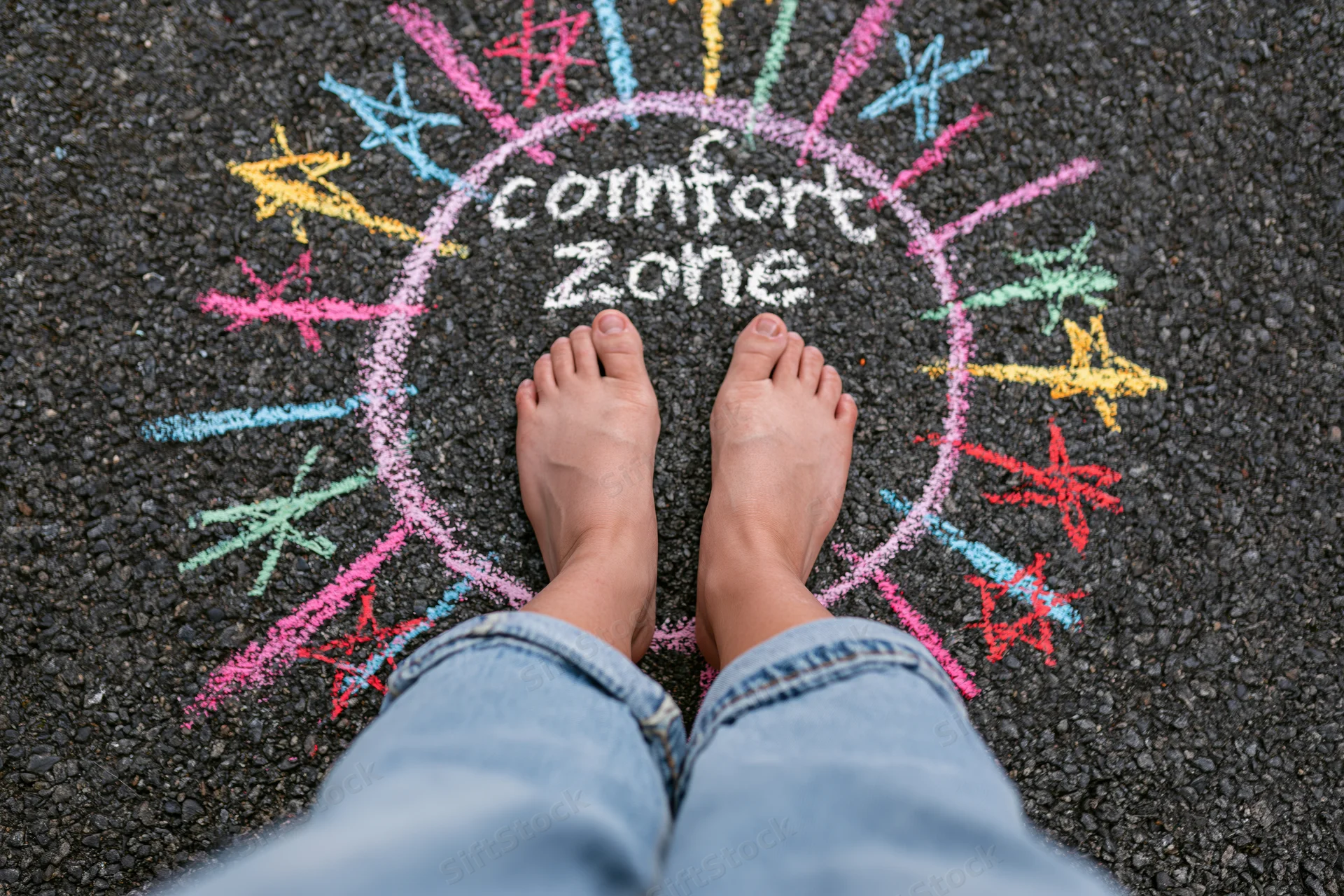 Bare feet standing inside a chalk-drawn circle labeled comfort zone on asphalt pavement