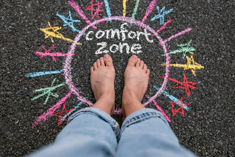 Bare feet standing inside a chalk-drawn circle labeled comfort zone on asphalt pavement