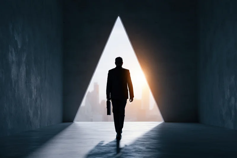 Businessman in suit walking toward triangular doorway with cityscape and sunset beyond