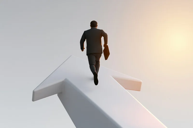 Businessman in suit running with briefcase on upward arrow toward sunrise