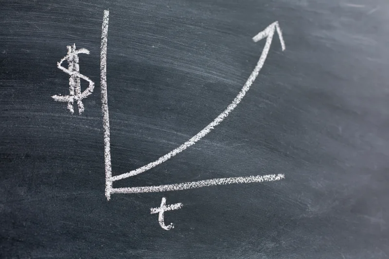 Chalk-drawn exponential growth graph on a blackboard with dollar symbol and time axis