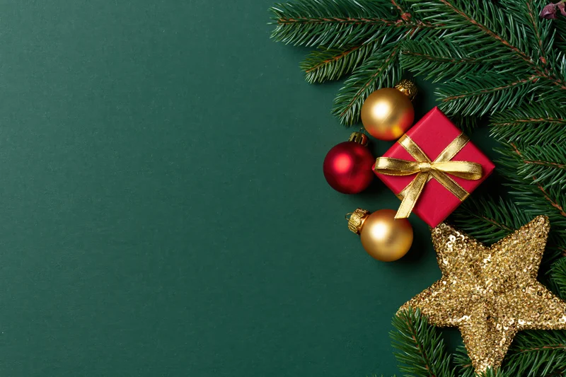 Christmas decorations including pine branches, red gift box, gold ornaments and star on green background with copyspace