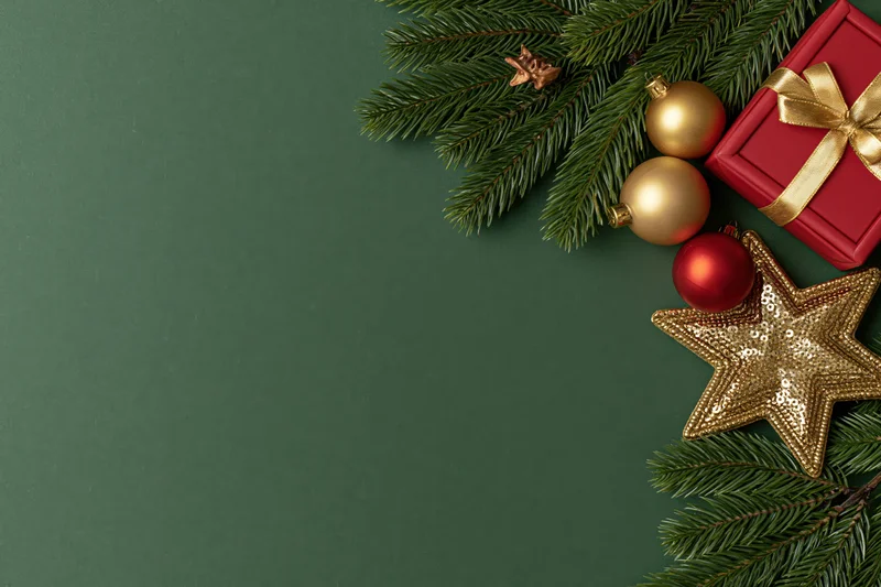 Christmas decorations and gift box arranged on green surface with copyspace