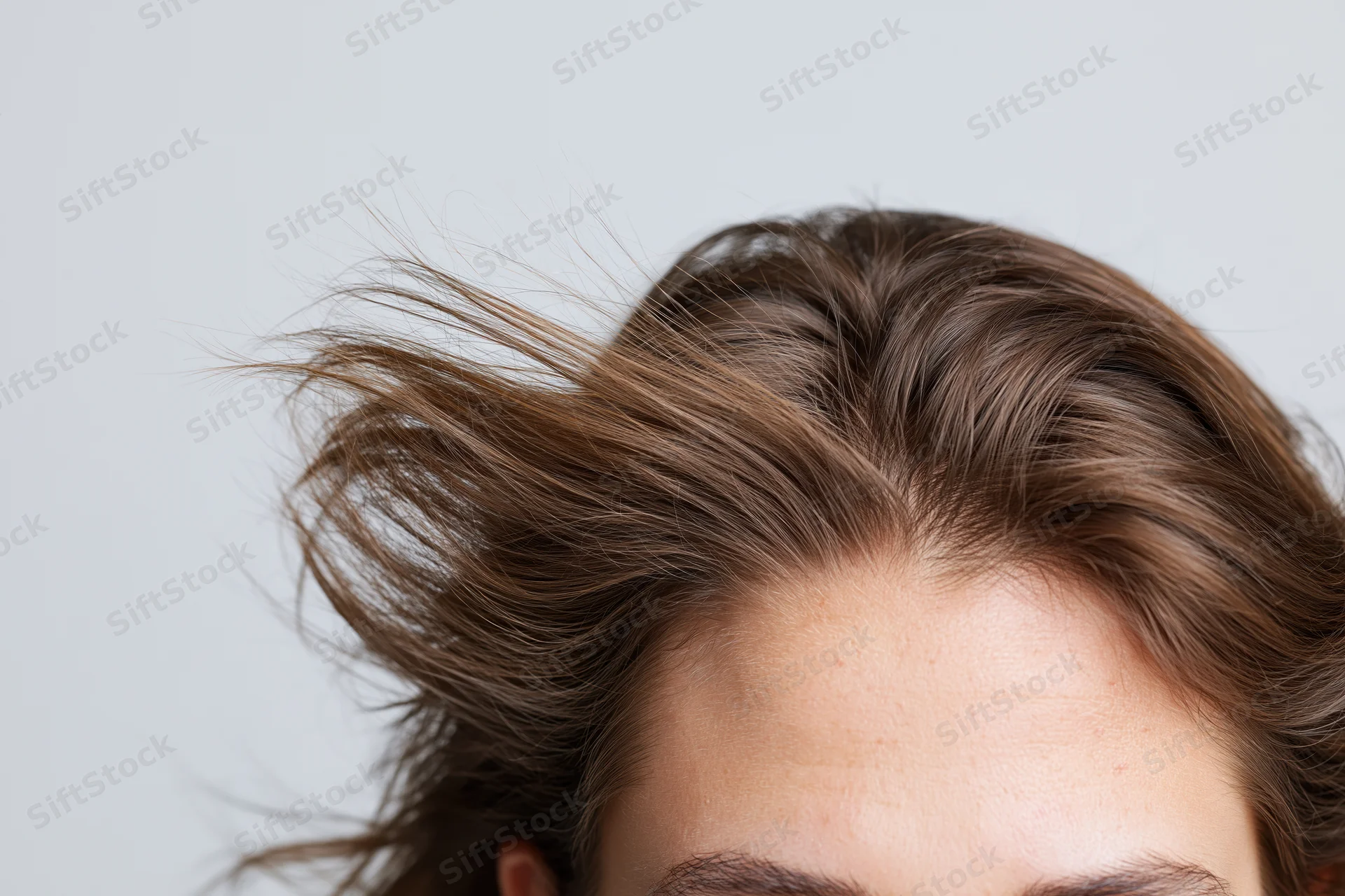 Close-up of a woman's head showing brown hair with flyaways and parting against a light background