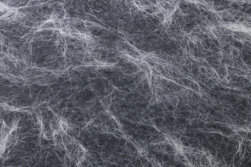 Tangled white fibers and fine lint on dark fabric surface