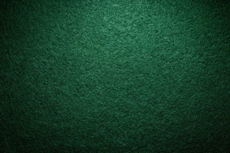 Close-up of green felt poker table surface with textured grain and dim lighting