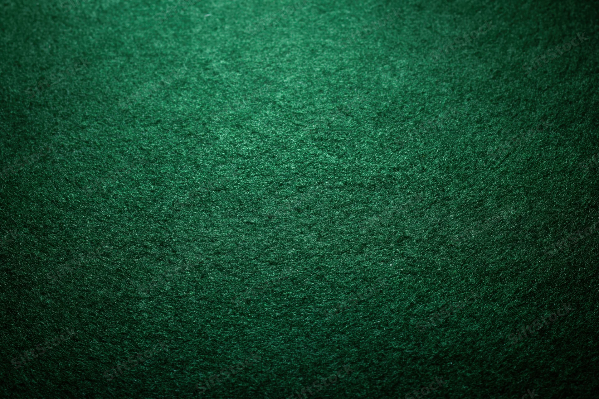 Close-up of green felt poker table surface with textured fabric and dim ambient lighting