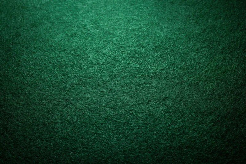 Close-up of green felt poker table surface with textured fabric and dim ambient lighting