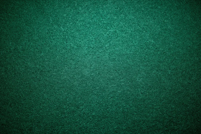 Close-up of green felt poker table surface with textured grain and subtle shadows