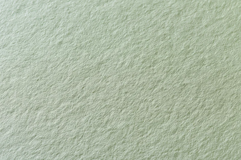 Close-up of a single sheet of pale sage green matte paper lying flat, showing its textured surface and even tone