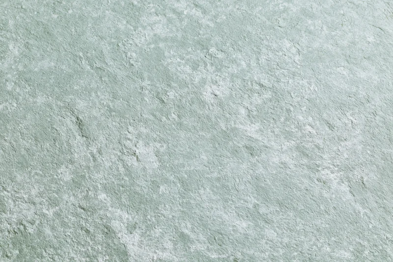 Close-up of a weathered concrete wall surface with textured gray and mint green finish