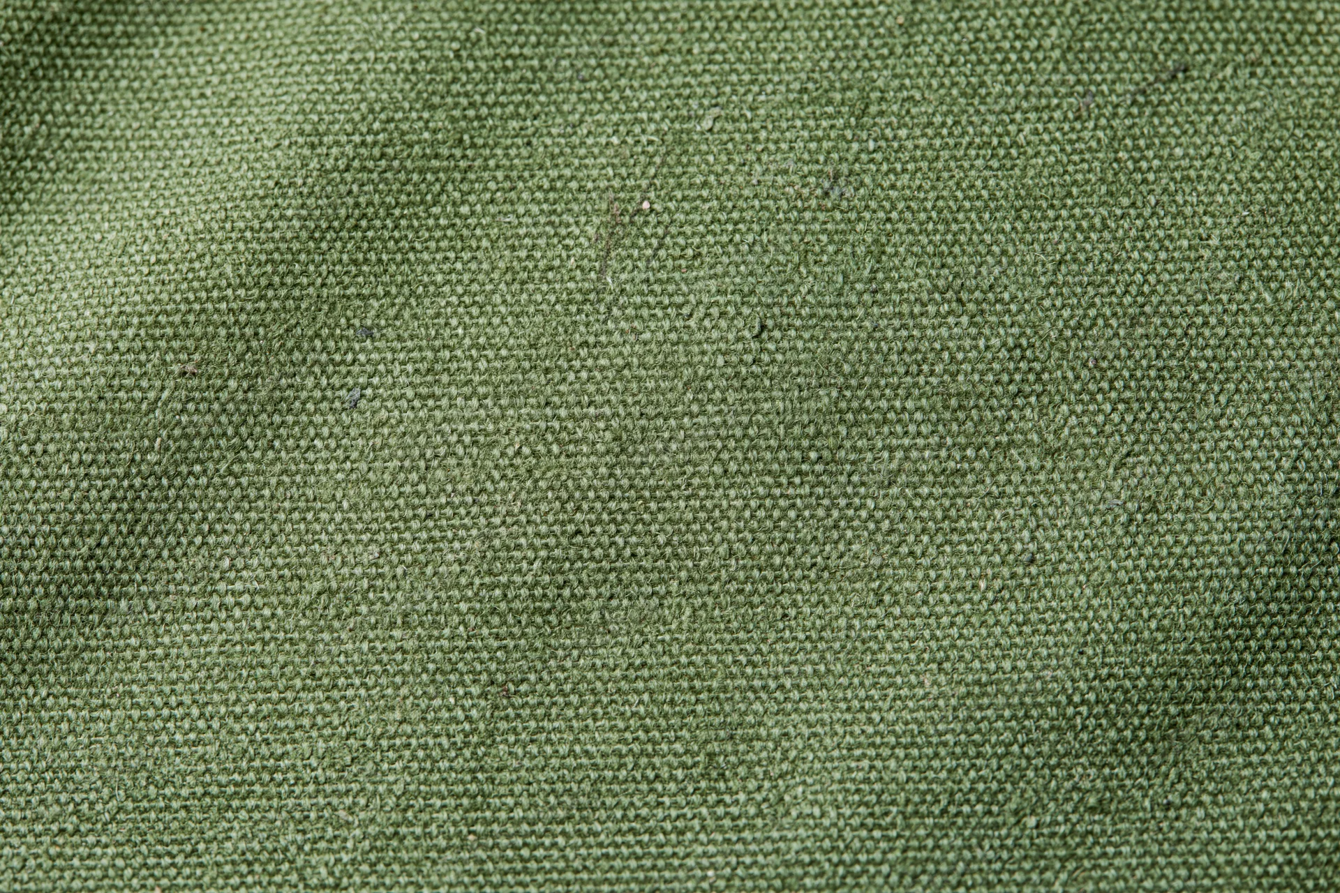 Close-up of aged olive green canvas fabric surface with visible weave and texture