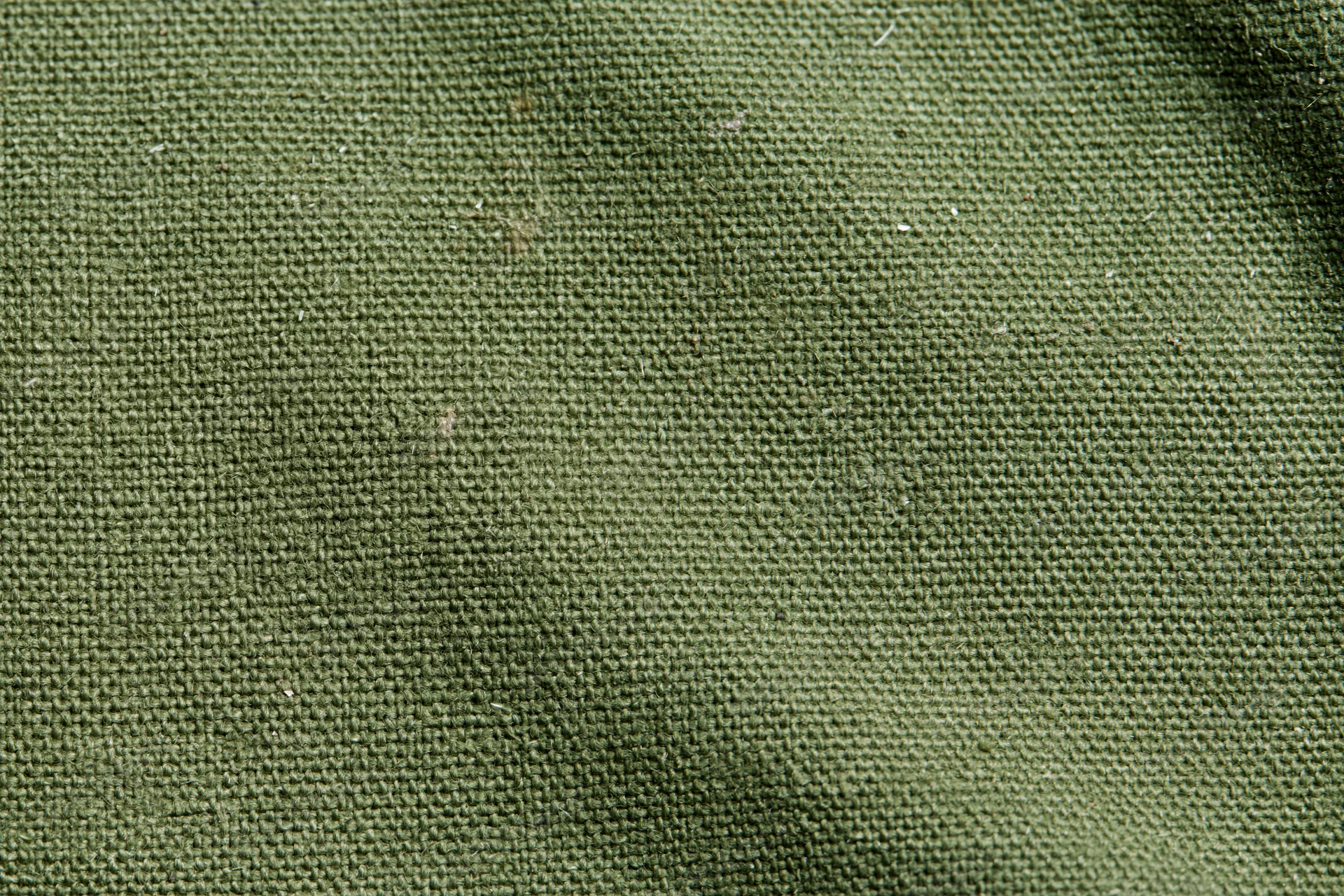 Close-up of aged olive green canvas fabric surface with visible weave and texture