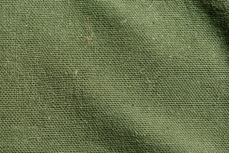 Close-up of aged olive green canvas fabric surface with visible weave and texture