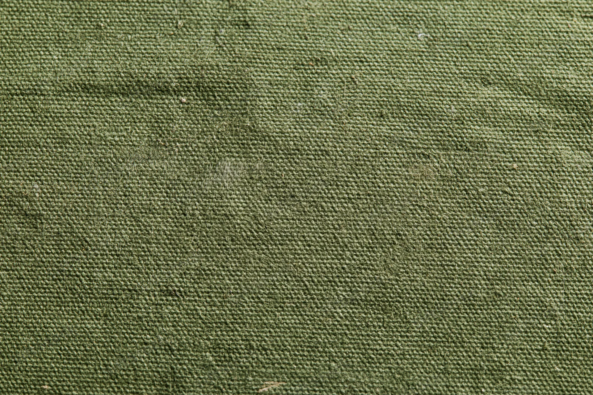 Close-up of aged olive green canvas fabric surface with visible weave and texture