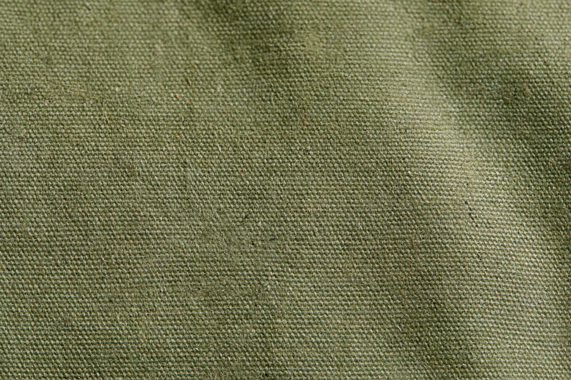 Close-up of aged olive green canvas fabric surface with visible weave and texture