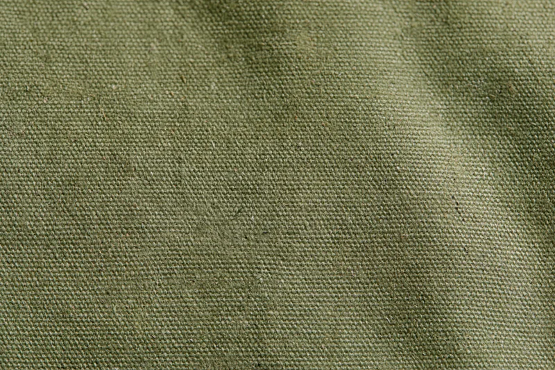 Close-up of aged olive green canvas fabric surface with visible weave and texture