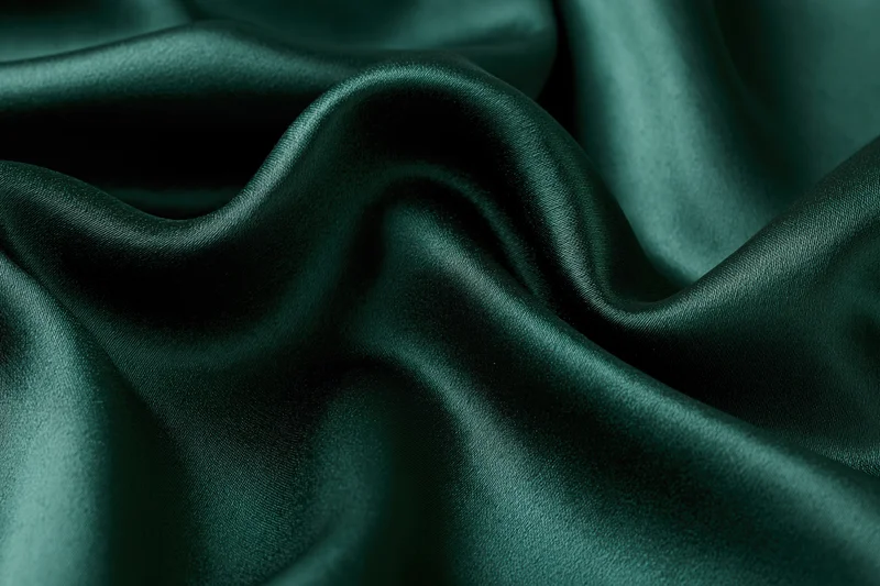 Close-up of dark emerald green satin fabric with soft folds and glossy texture