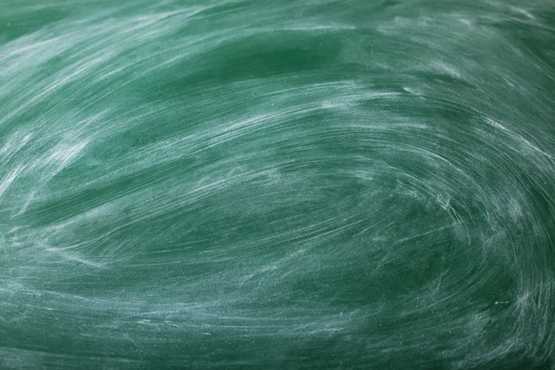 Close-up of a green chalkboard surface with smudged white chalk marks and swirl patterns from erasing