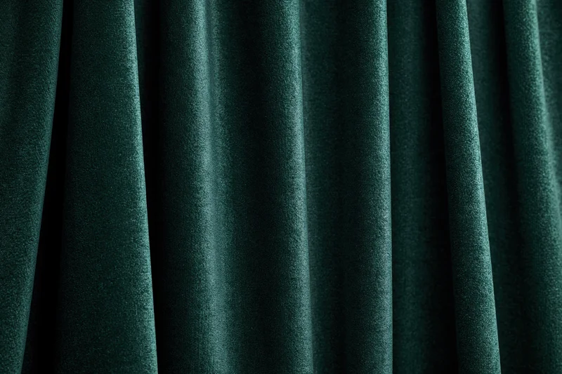 Close-up of heavy dark emerald green velvet curtain with deep folds and rich texture