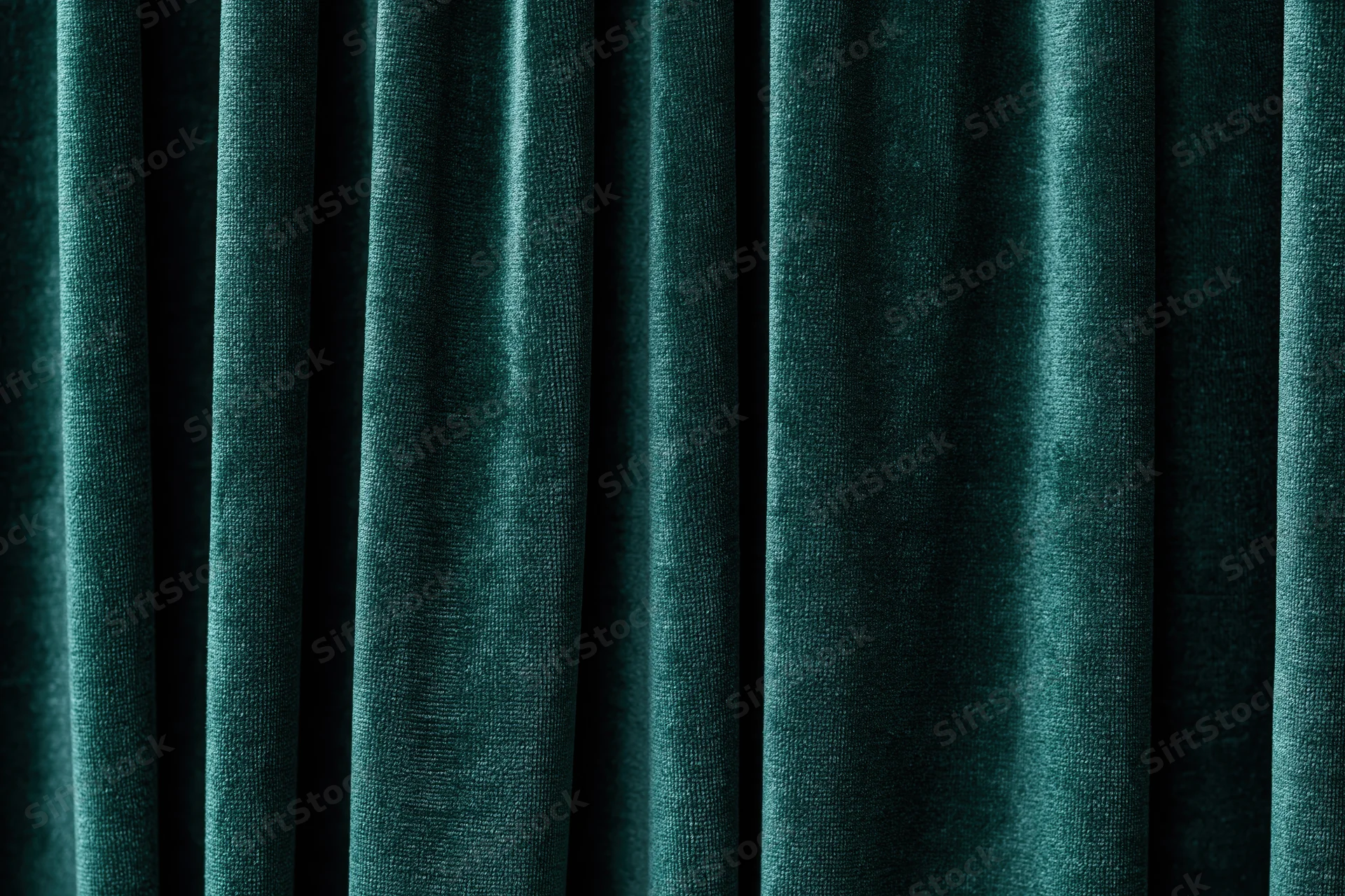 Close-up of heavy dark emerald green velvet curtain with deep folds and rich texture