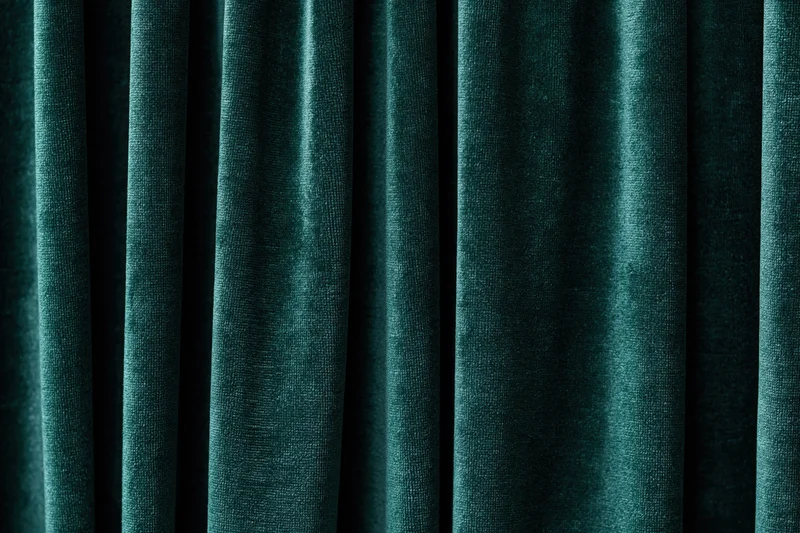 Close-up of heavy dark emerald green velvet curtain with deep folds and rich texture