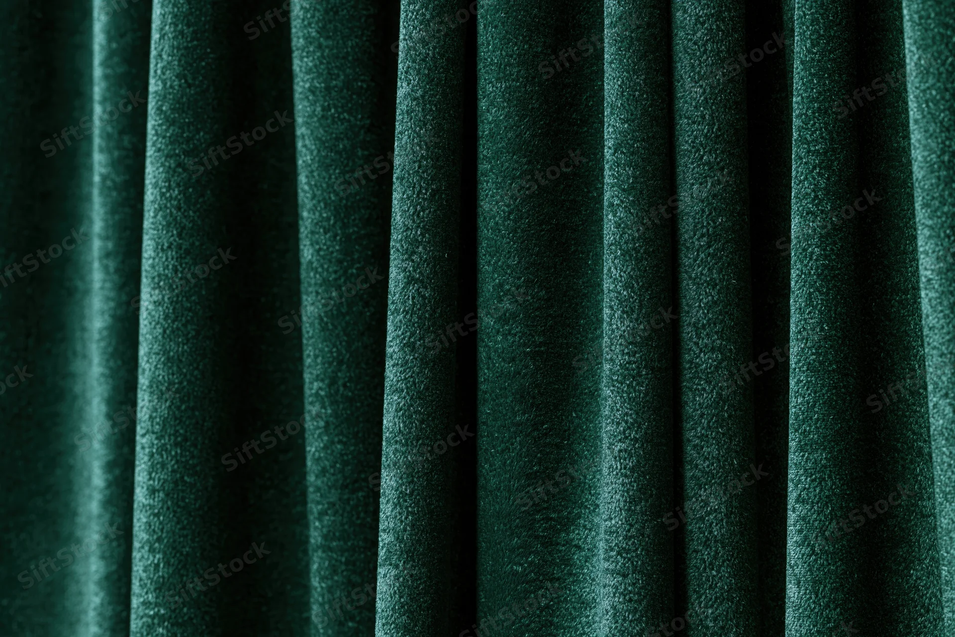 Close-up of dark emerald green velvet curtain with vertical folds and soft texture