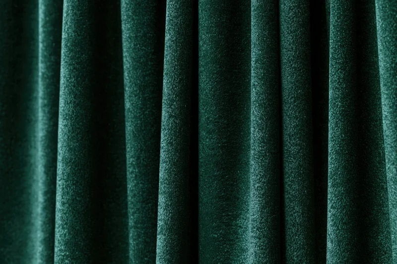 Close-up of dark emerald green velvet curtain with vertical folds and soft texture