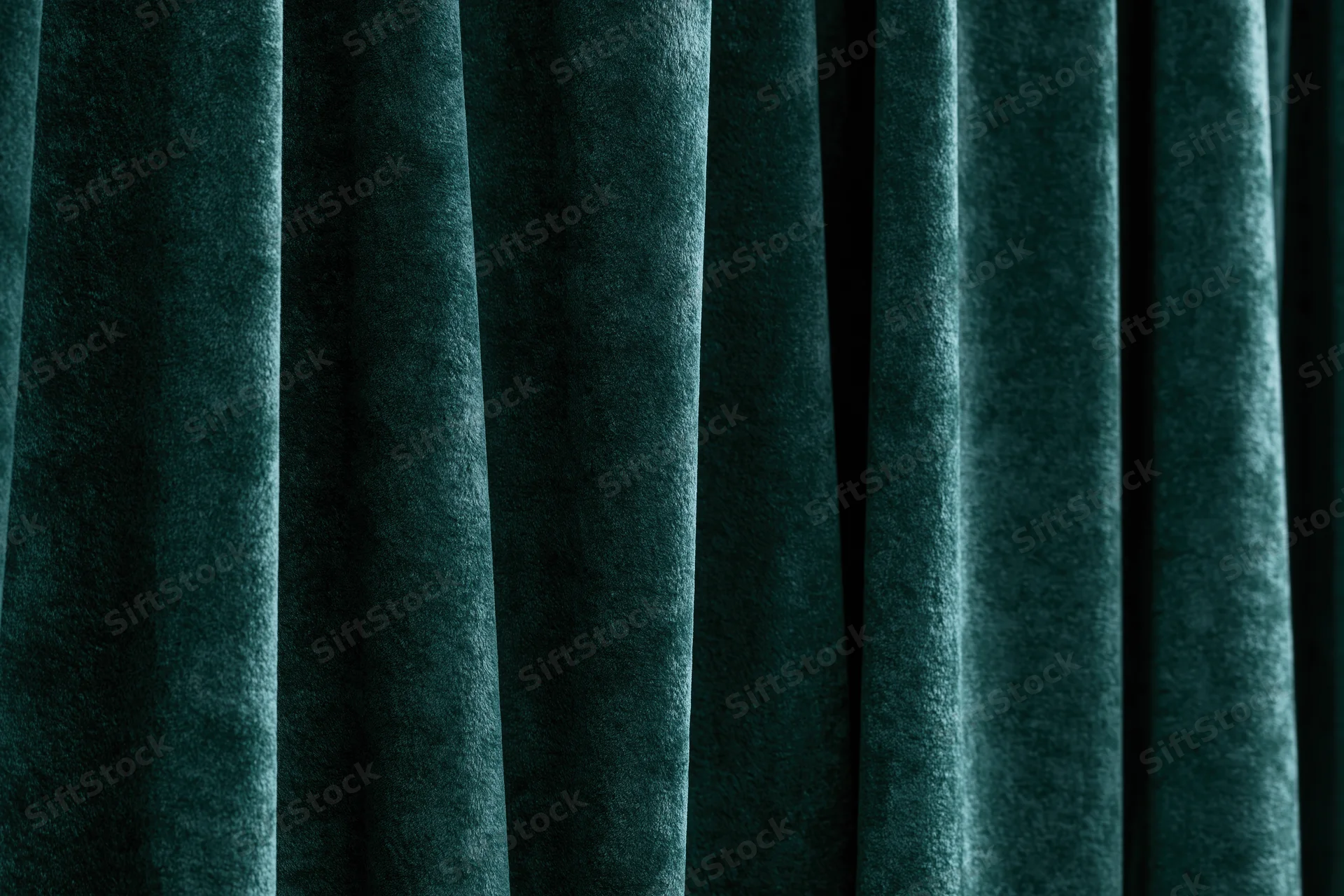 Close-up of heavy dark emerald green velvet curtain with vertical folds and soft texture