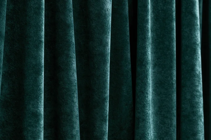 Close-up of heavy dark emerald green velvet curtain with vertical folds and soft texture