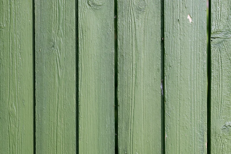Vertical green painted wooden planks showing weathered texture and grain as outdoor fence surface