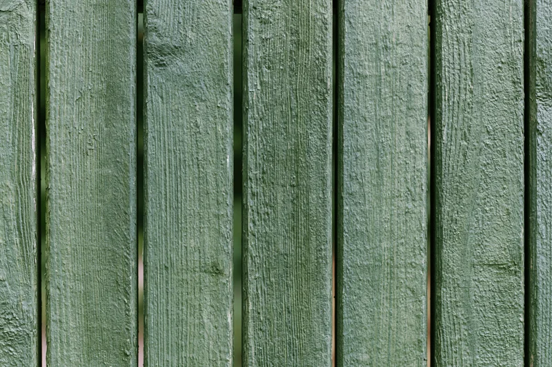 Vertical green painted wooden planks forming a weathered outdoor fence surface